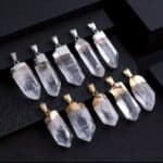 Clear quartz crystal pendants with silver-tone caps arranged in two rows on a black display backdrop, showcasing multiple shapes and facets.