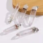Clear quartz crystal pendants with silver caps and loops, laid out on a white surface with a wooden board nearby