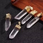 Clear quartz crystal pendants with gold-tone caps arranged on a dark fabric background, jewelry pieces for sale or collection.
