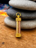 Gold cylindrical pendant with knurled ends and two engraved tubes inside, suspended from a circular bail atop stacked stones.