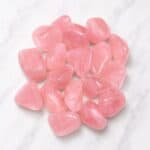 Pink rose quartz tumbled stones arranged in a cluster on a white marble surface on display for decoration/collection.