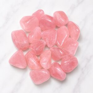 Pink rose quartz tumbled stones arranged in a cluster on a white marble surface on display for decoration/collection.