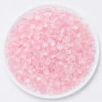 Pile of small pink glassy gemstones on a white plate, resembling rose quartz chips.