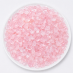 Pile of small pink glassy gemstones on a white plate, resembling rose quartz chips.