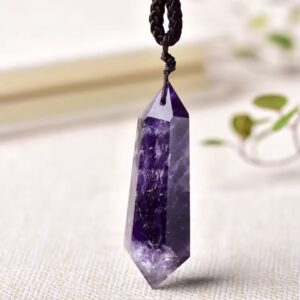Purple amethyst crystal pendant hanging on a braided black cord against a soft background.