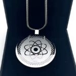 Metallic circular pendant featuring an atomic model on a chain, displayed in a dark jewelry case.