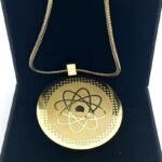 Gold circular pendant with atomic symbol on a blue jewelry box, hanging from a gold chain.