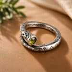 Silver spiral ring with a green faceted gemstone and engraved symbols on orange satin fabric.
