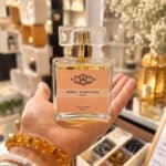 Perfume bottle with pink label reading Neroli - Ylang Ylang, held in a shopper's hand in a fragrance shop.