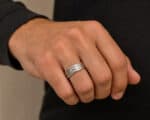 Close-up of a hand wearing a silver multi-band ring on the ring finger; dark sleeve visible in the background.
