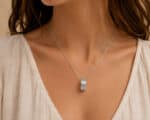 Close-up of a silver layered ring pendant on a delicate chain resting on a woman's collarbone area.