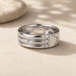 Silver multi-band ring resting on sandy surface with a blurred stone in the background.