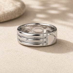 Silver multi-band ring resting on sandy surface with a blurred stone in the background.