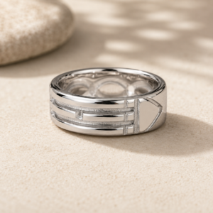 Silver multi-band ring resting on sandy surface with a blurred stone in the background.