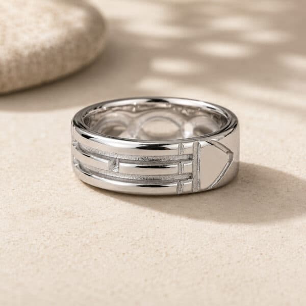 Silver multi-band ring resting on sandy surface with a blurred stone in the background.