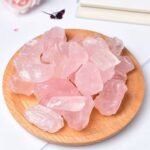 Pink rose quartz chips scattered on a round wooden plate against a light background.