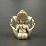 Brass seated figurine in a meditative pose, viewed from the back with hands raised in mudras.
