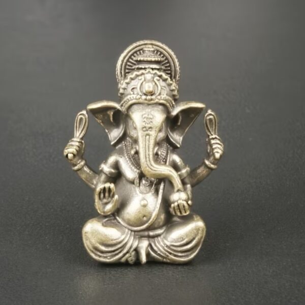Metallic statue of the Hindu god Ganesha, seated cross-legged with four arms and a crown against a dark background