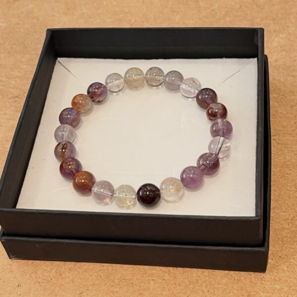 Beaded bracelet with translucent purple, pink, and amber beads arranged in a circle inside a black jewelry box on a white tray.