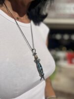Close-up of a person wearing a turquoise and silver pendant necklace over a white ribbed top.