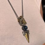 Metallic layered necklaces with ornate pendants resting on pale pink ribbed fabric.