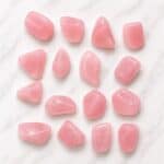 Pink rose quartz tumbled stones arranged on a white marble surface
