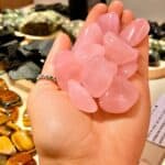 Hand cupping several pink rose quartz tumbled stones, with a ring on the finger, in a gem display