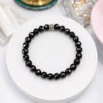 Black faceted bead bracelet displayed on a white circular stand or surface.