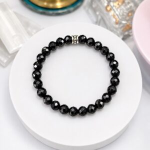 Black faceted bead bracelet displayed on a white circular stand or surface.