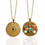 Two gold circular pendant necklaces: left shows an atomic orbital pattern, right displays multicolored gems set in circles on a gold disc.