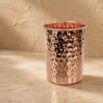 Hammered copper tumbler with a pinkish interior on a light stone surface.