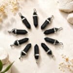 Nine black crystal pendants with silver caps arranged in a circle on a beige stone surface.