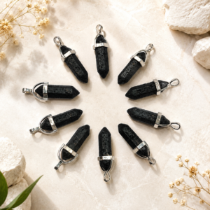 Nine black crystal pendants with silver caps arranged in a circle on a beige stone surface.